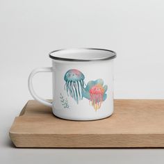 a white coffee mug with jellyfish and seaweed on it sitting on a wooden tray