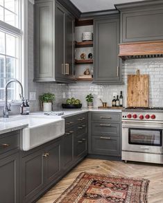 a kitchen with gray cabinets and white marble counter tops, an area rug on the floor