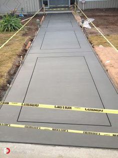 a concrete walkway being laid in front of a building with yellow tape on the ground