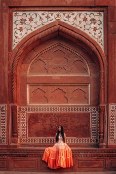 a woman in an orange dress is sitting on the ground near a wall and doorway