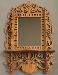 a wooden mirror and shelf on the wall with an ornate design around it's edge