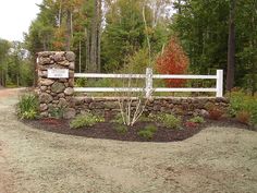 a stone wall and white fence in front of a wooded area with trees, shrubs and flowers