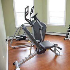 there is a gym equipment set up in the room with hard wood flooring and windows