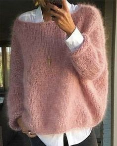 a woman wearing a pink sweater and black pants is looking at her cell phone while standing in front of a door