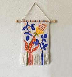 an embroidered wall hanging with flowers and leaves