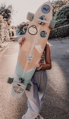 a person holding a skateboard with stickers on it's face and standing in the street