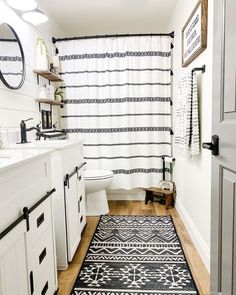 a bathroom with a black and white rug on the floor next to a shower curtain