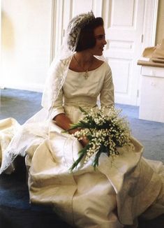 a woman sitting on the floor in a wedding dress holding a bouquet of white flowers