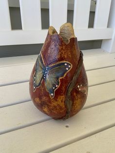 a vase with a butterfly painted on it sitting on a white porch table next to a fence