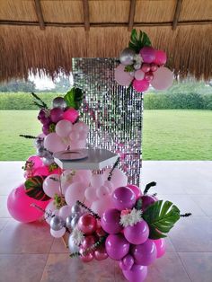 a table topped with balloons and flowers on top of a tile floor next to a grass covered roof