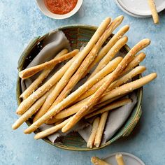 some bread sticks are in a bowl on a blue table with sauces and napkins