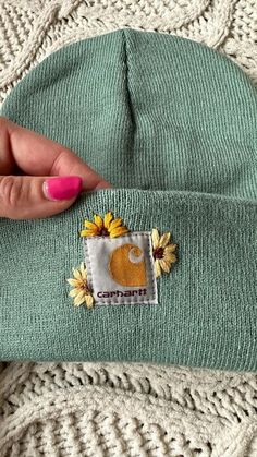 a woman's hand holding onto a green beanie with sunflowers on it