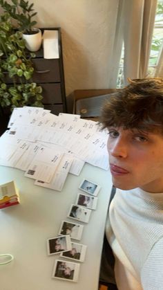 a young man sitting at a desk in front of a white table with pictures on it