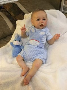 a baby laying on top of a white blanket next to a blue stuffed animal toy