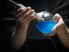 a person holding a blue liquid in their hand and pouring it into a glass bowl