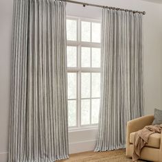 a living room filled with furniture and a large window covered in striped drapes next to a chair