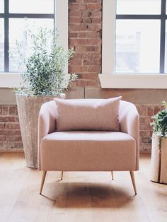 a pink chair sitting in front of two potted plants next to a brick wall