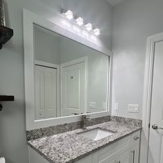 a white bathroom with granite counter tops and large mirror above the sink, along with two lights on either side of the door