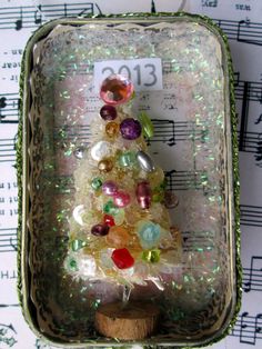 a small christmas tree made out of glass beads in a tin container with sheet music notes