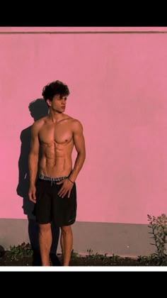 a man standing in front of a pink wall with his shirt off and no shirt on