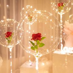 two clear vases with red roses in them and some lights on the wall behind them