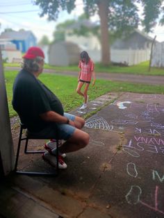 two children are sitting in chairs on the sidewalk with chalk writing all over the ground