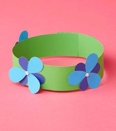 a green and blue paper flower bracelet on a pink background with two flowers in the center