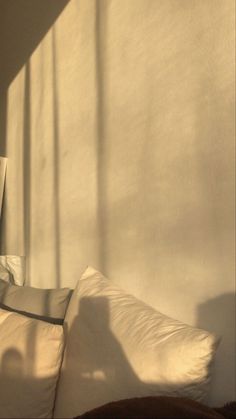 a bed with white sheets and pillows in front of a light shining on the wall