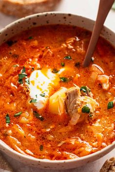 a bowl of soup with meat and cheese in it next to bread on the side