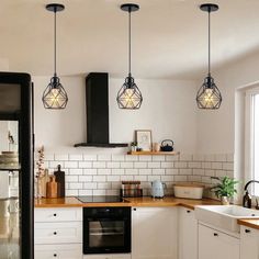 three lights hanging from the ceiling in a kitchen with white cabinets and wood counter tops