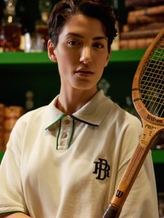 a young man holding a tennis racket in his right hand and looking at the camera