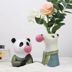 two ceramic panda bears sitting next to each other with flowers in the vase behind them