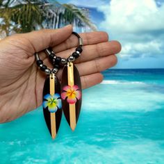 🌺 Aloha! Embrace the spirit of the islands with our beautifully handcrafted Surfboard Necklace featuring a vibrant Hawaiian flower painted in the center. This unique and eye-catching piece is perfect for beach lovers, surfers, or anyone who appreciates the beauty of tropical paradise. 🌊 Surfboard Pendant: Made of high-quality wood, this lightweight pendant measures 2.5 inches long and showcases a stunning, hand-painted Hawaiian flower design that adds a touch of color and charm to any outfit. 📿 Necklace: The 18-inch necklace features a durable and comfortable cord that fits most sizes, making it suitable for both men and women. The lobster claw closure ensures a secure and easy fit, while the adjustable cord allows for a customized length that complements your style. 🎁 Unisex Design: O Bohemian Flower Charm Jewelry For Beach, Multicolor Flower Jewelry For Beach, Multicolor Tropical Jewelry For Beach, Tropical Style Multicolor Jewelry For Beach, Tropical Multicolor Beach Jewelry, Tropical Style Multicolor Jewelry As Gift, Surfer Girl Necklace, Surfer Girl Jewelry, Surf Necklace