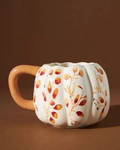 an orange and white ceramic coffee mug on a brown surface with leaves painted on it