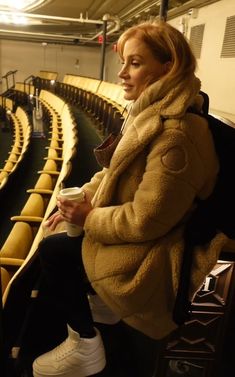 a woman sitting on a bench in front of a row of empty seats holding a cup