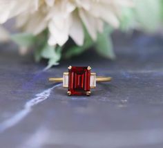 a red and white diamond ring sitting on top of a table next to a flower