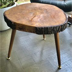 a wooden table sitting on top of a floor next to a black leather chair and potted plant