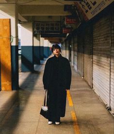 a woman is walking down the sidewalk with a handbag in her other hand while wearing a long black coat