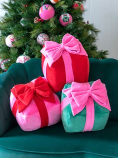 three wrapped presents sit on a green chair in front of a christmas tree with ornaments