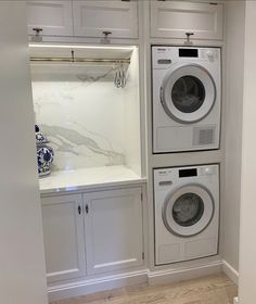 a washer and dryer in a white laundry room with built - in cabinets