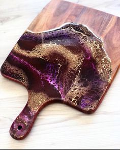 a wooden cutting board with a purple and gold design on the top, sitting on a white surface