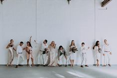 a group of people standing next to each other in front of a white wall holding bouquets