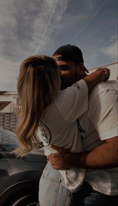 a man and woman embracing each other in front of a car with the sky behind them