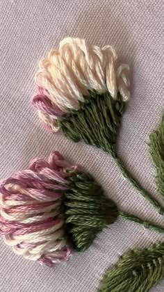 three flowers that are on top of a cloth tablecloth, one is pink and the other is green