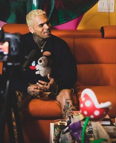 a man sitting on top of a couch holding a stuffed animal next to a camera