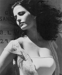 a black and white photo of a woman with her hair blowing in the wind, wearing a bra