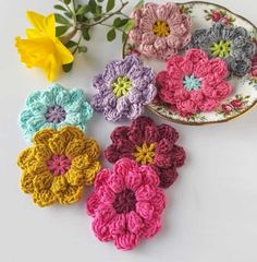 small crocheted flowers sitting on top of a white table next to yellow and pink flowers