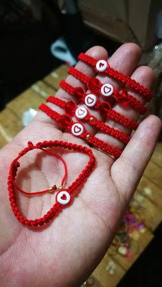 a hand holding several red string bracelets with white hearts on them and one beaded heart in the middle