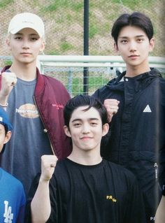 four young men standing next to each other in front of a metal fence with their fists raised