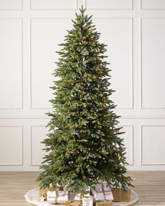 a christmas tree with presents under it on a wooden floor in front of a white wall